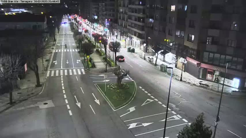 A nighttime aerial view shows a city street intersection with minimal traffic, surrounded by buildings and streetlights.
