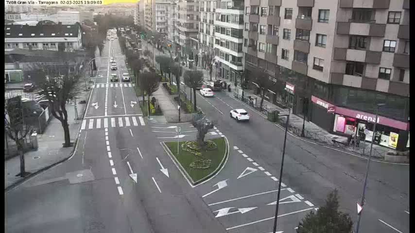 A city street with several cars driving on it under a mostly clear sky.