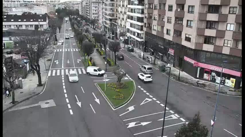A city street intersection with several cars and buildings on an overcast day.
