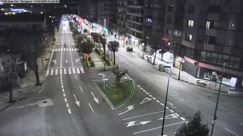 A mostly empty city street at night, with some cars visible in the distance and streetlights illuminating the road and surrounding buildings.