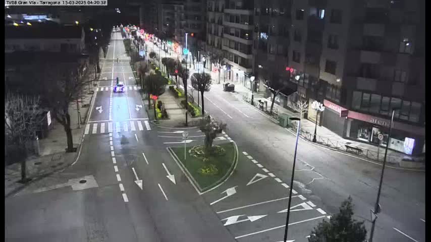 A mostly empty, well-lit street at night, with a few cars and trees lining the sides, under clear skies.