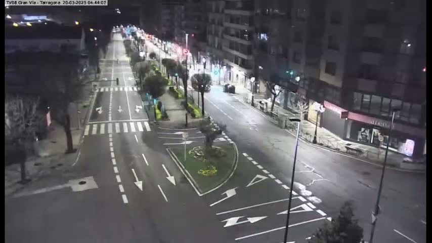 A mostly empty, well-lit street at night, showing several intersections and buildings along the sides.