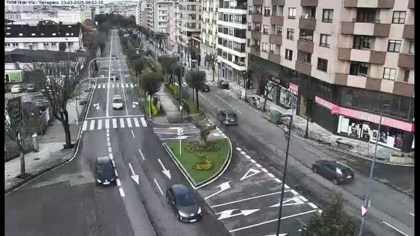 A wide shot of a city street with several cars driving on a multi-lane road under a cloudy sky.