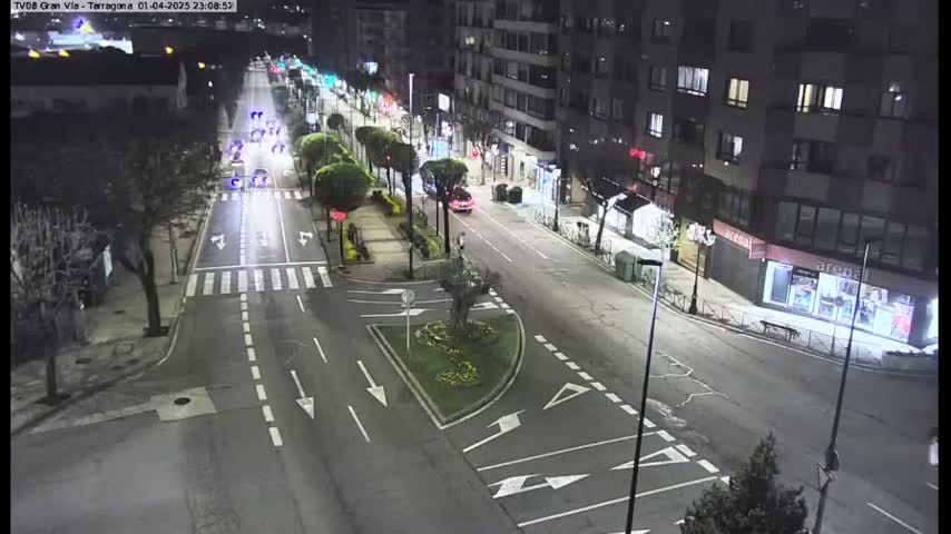 A nighttime street scene shows a multi-lane road with sparse traffic, intersecting with other roads, surrounded by buildings and streetlights.
