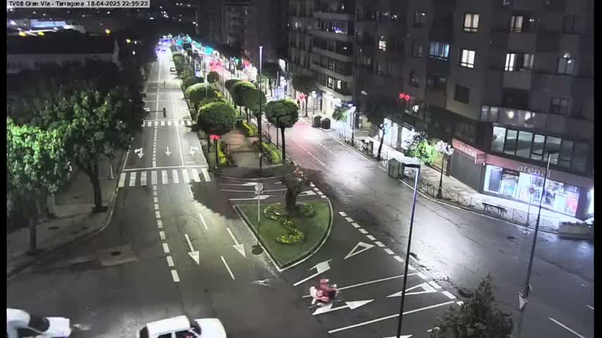 A nighttime, high-angle view of a mostly empty city street with cars and trees lining the sides, under streetlights.