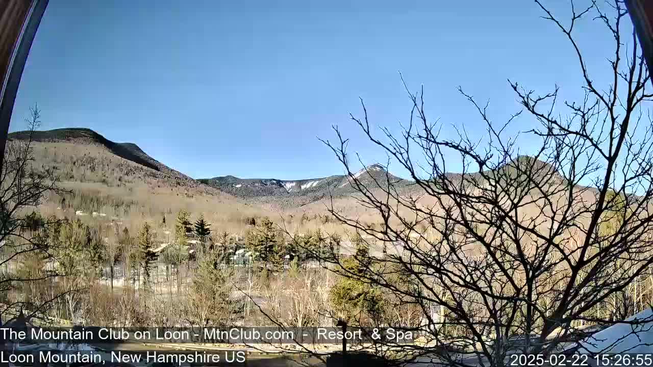 A view through a window shows a sunny, snow-dusted mountain range in the distance, partially obscured by bare trees in the foreground.