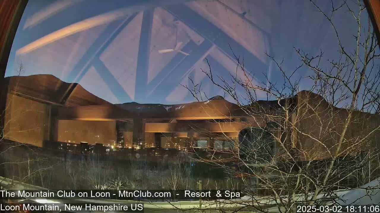 A nighttime view through a window shows a building illuminated against a mountain range under a twilight sky.