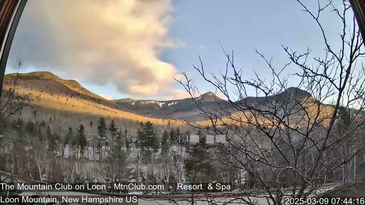 A view through a window shows a partly cloudy sunrise over snow-dusted mountains and a winter landscape.