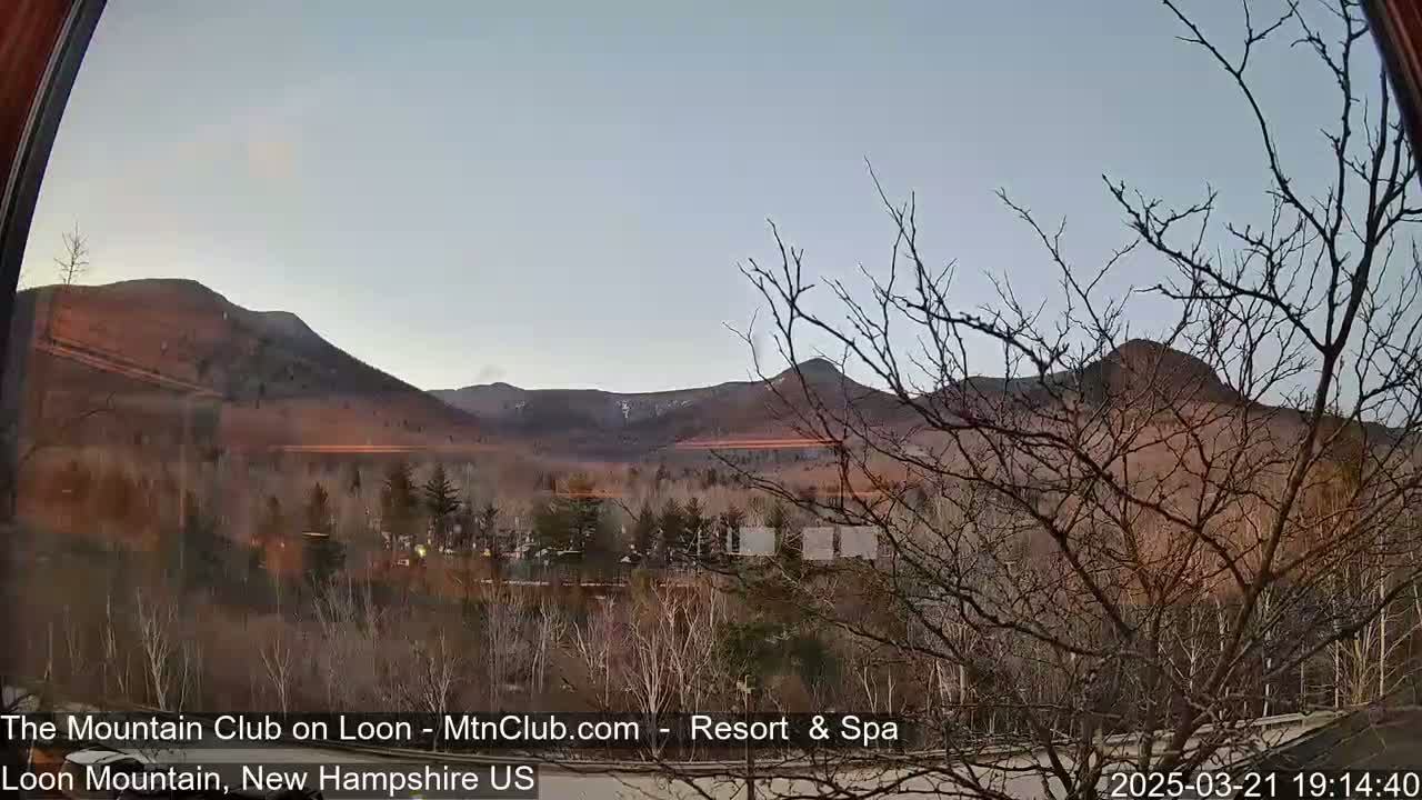 A view through a window shows bare trees in the foreground, a valley, and distant mountains under a twilight sky.
