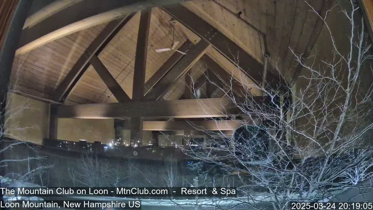 A nighttime view through a window shows a snow-covered landscape and the interior of a large, high-ceilinged building with exposed wooden beams and a ceiling fan.