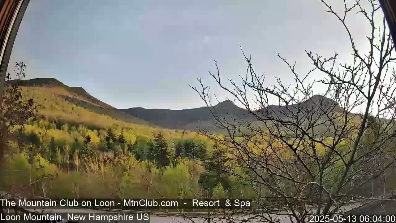 A view through a window shows a mostly clear sky over rolling hills and mountains covered in a mix of green and yellow trees.