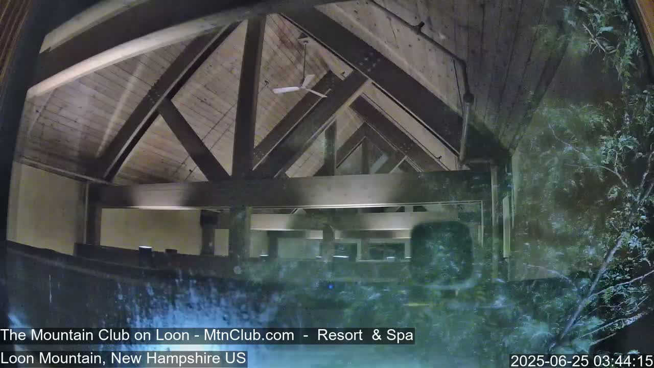 A view through a rain-streaked window shows the interior of a building with a high, wood-beamed ceiling and a ceiling fan.