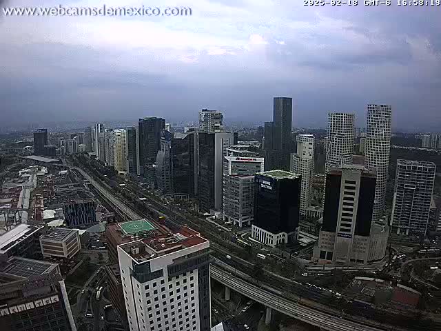 A high-angle, long shot of a cityscape on an overcast day shows many skyscrapers and a large highway.
