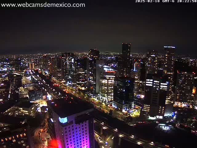 A nighttime aerial view of a brightly lit city with numerous skyscrapers and roadways under a clear, dark sky.