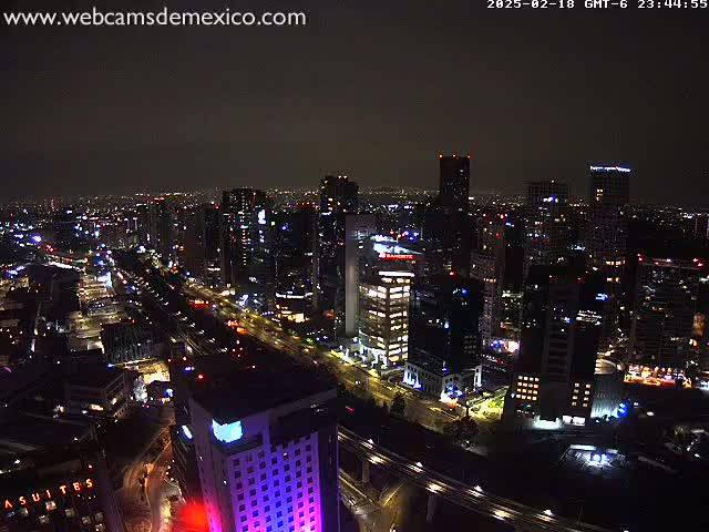A nighttime, aerial view of a city with many tall buildings and brightly lit roads under a dark, cloudy sky.