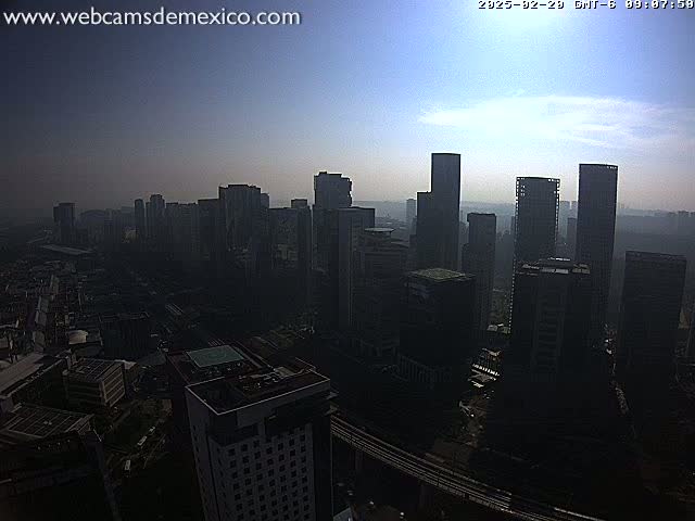 A hazy, sunlit cityscape of numerous dark skyscrapers and buildings stretches out, viewed from a high vantage point.