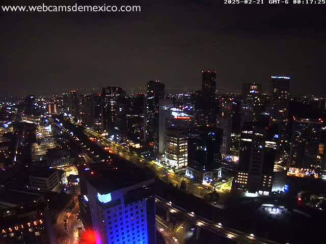 A nighttime aerial view of a city with numerous illuminated skyscrapers and roadways under a cloudy sky.