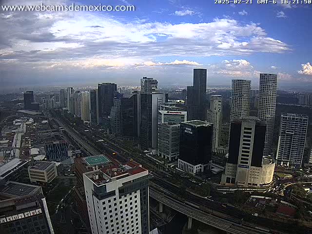A partly cloudy sky overlooks a large city with many skyscrapers and a busy highway below.
