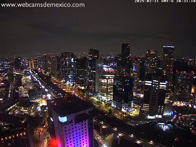 A nighttime aerial view of a city with brightly lit buildings and roadways under a partly cloudy sky.