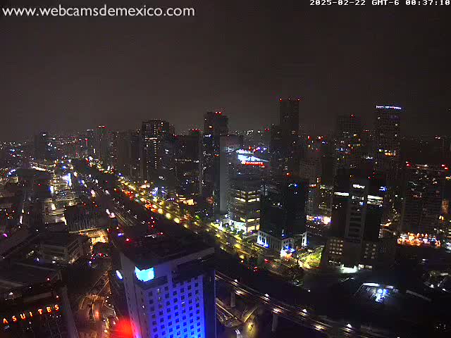 A nighttime aerial view of a city with many illuminated buildings and roadways under a dark, cloudy sky.