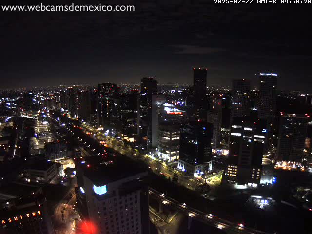 A nighttime aerial view of a city illuminated by lights, under a dark, cloudy sky.