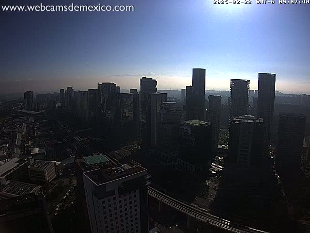 A hazy, sunlit cityscape of tall buildings is viewed from a high vantage point.