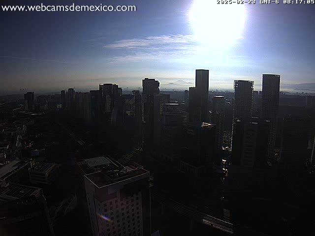 A hazy sunrise illuminates a cityscape of numerous tall buildings, casting long shadows.