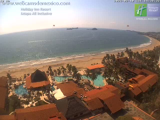 An aerial view of a resort on a sandy beach with a calm ocean under a clear sky.