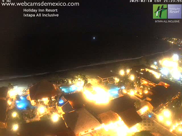 A brightly lit resort at night next to a dark ocean under a clear sky.
