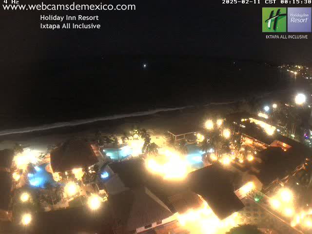 A brightly lit resort at night, next to a dark ocean under a clear sky.