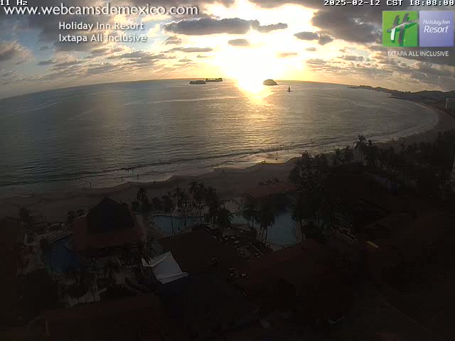 An ocean beach scene at sunset, with palm trees, a resort, and swimming pools visible from an elevated viewpoint.