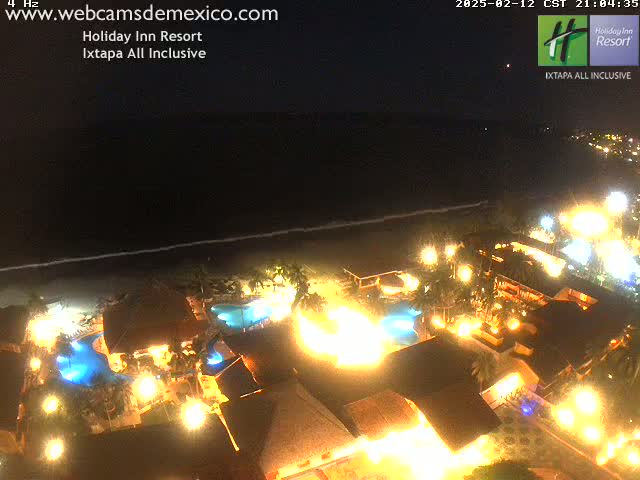 A brightly lit resort at night, next to a dark ocean under a clear sky.