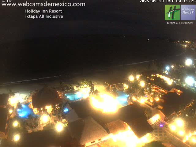 An illuminated resort at night, situated on a beach next to a dark ocean.