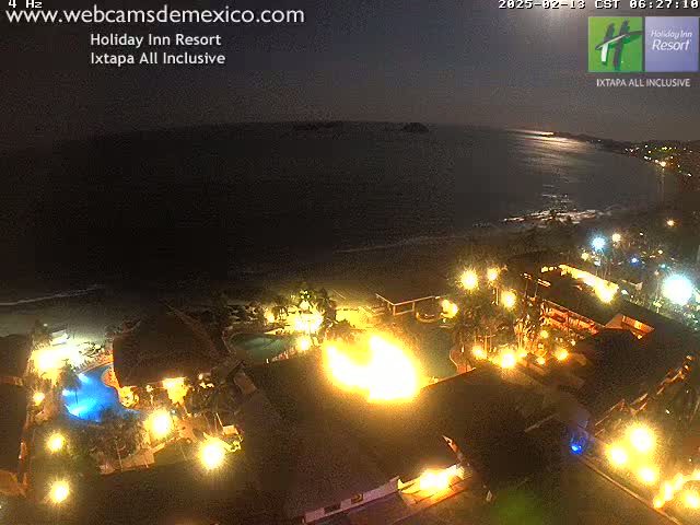 A brightly lit resort at night overlooks a dark ocean under a moonlit sky.