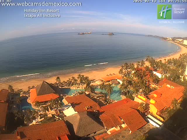 An aerial view of a resort on a sandy beach with calm ocean under a mostly clear sky.