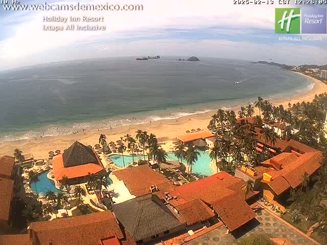 An aerial view of a resort complex on a sandy beach with calm ocean waters under a partly cloudy sky.