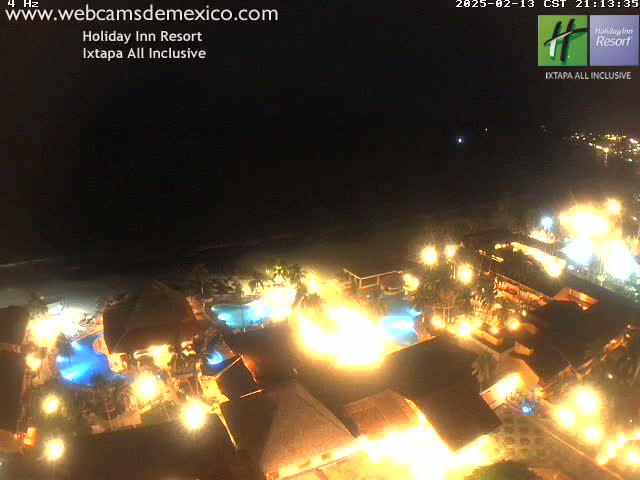 A brightly lit resort at night, situated near a dark ocean under a clear sky.
