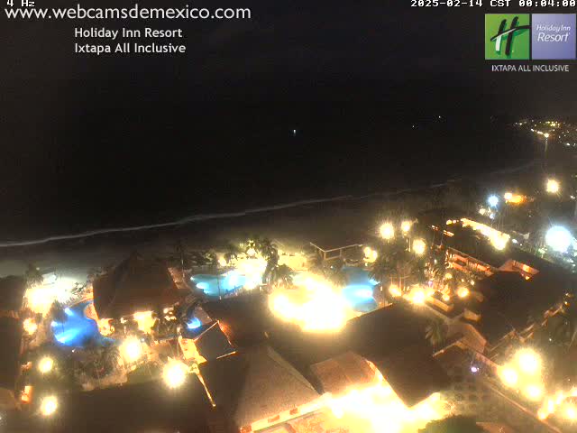 A nighttime aerial view of a brightly lit resort complex next to a dark ocean under a clear sky.