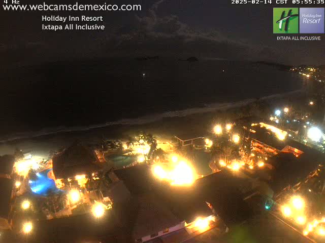 A brightly lit resort at night overlooks a dark ocean under a mostly clear sky.