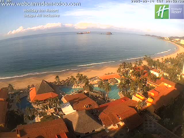 An aerial view of a resort on a sandy beach next to a calm ocean under a mostly clear sky.