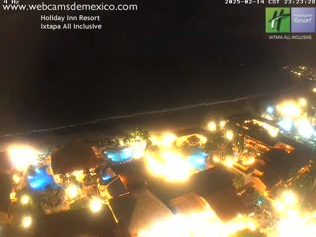 A brightly lit resort complex at night next to a dark ocean under a clear sky.