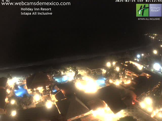 A brightly lit resort at night, situated next to a dark ocean under a clear sky.