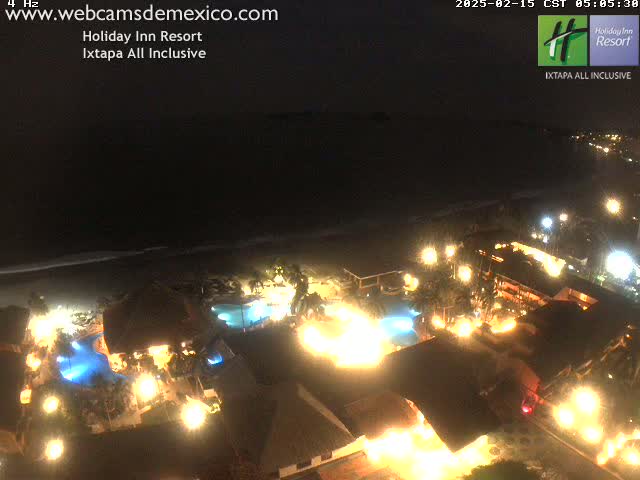 A brightly lit resort at night, situated on a beach under a dark sky.