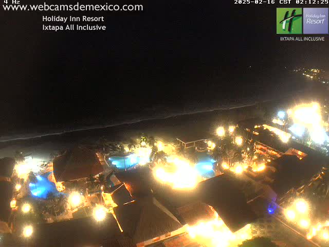 A brightly lit resort at night, situated next to a dark ocean under a clear sky.