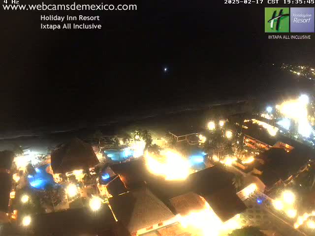 A brightly lit resort at night, nestled near a dark ocean under a clear sky.