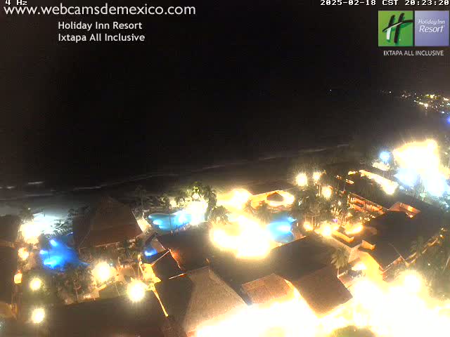 A brightly lit resort at night, next to a dark ocean under a clear sky.