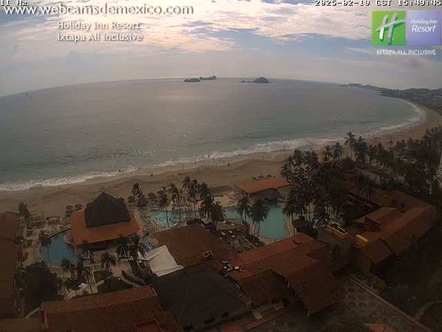An aerial view of a resort on a beach with calm ocean water under a partly cloudy sky.