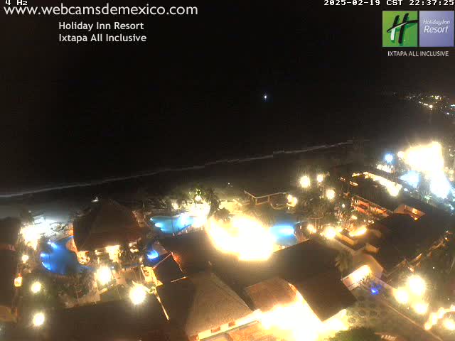 A brightly lit resort complex at night, situated on a coastline under a dark, clear sky.