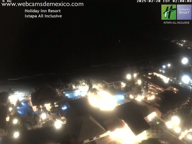 A brightly lit resort at night sits next to a dark ocean under a clear sky.