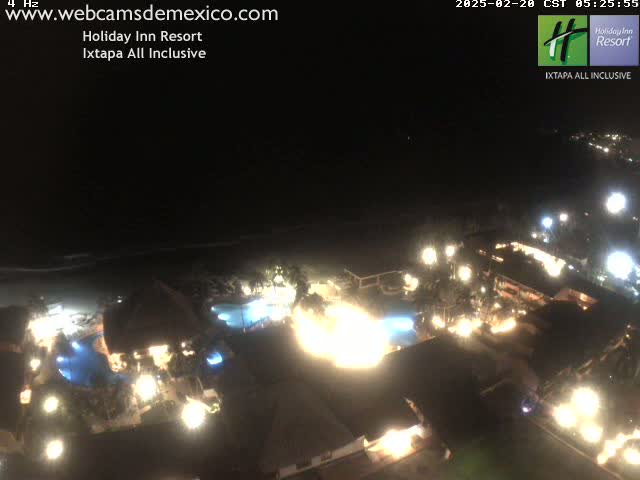A brightly lit resort at night, situated near a dark ocean under a clear sky.